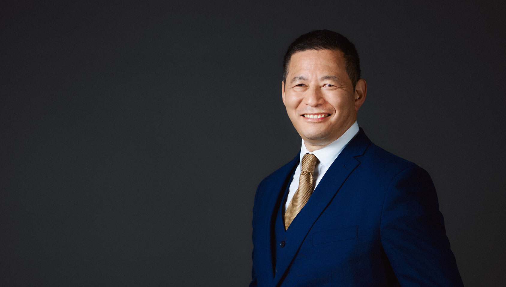 A man smiling, dressed in a blue suit