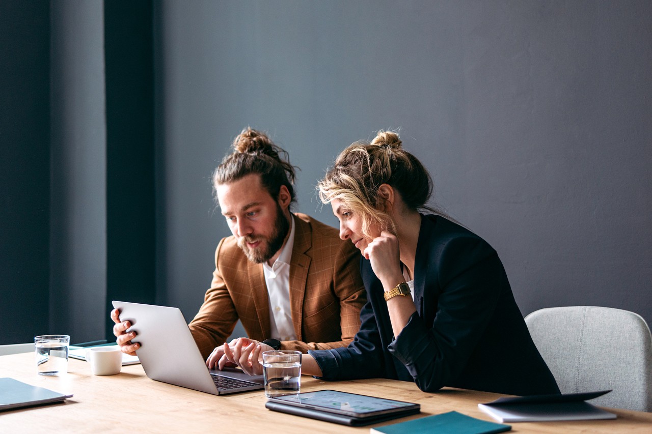 Happy businessman and businesswoman using a laptop computer while talking and sitting together at office desk.